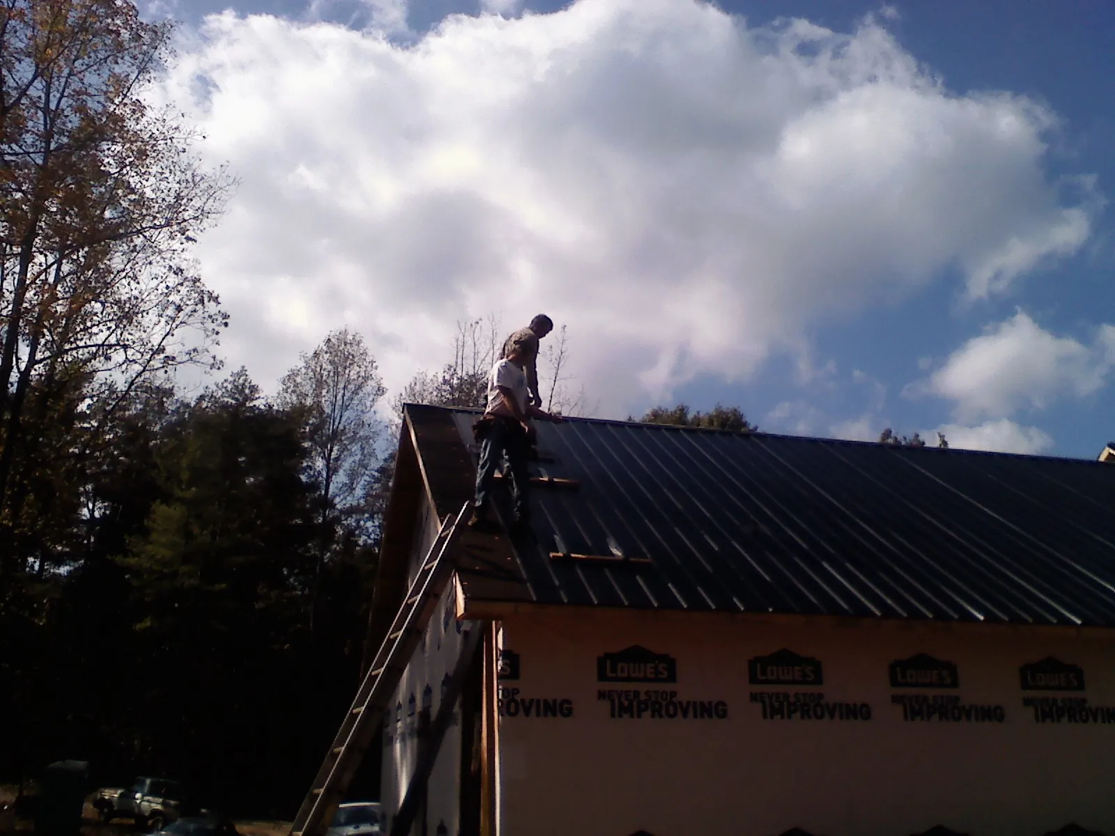Roofer fastening dark metal panels high against a cloudy sky, from a Roof Inspection job in Reedville
