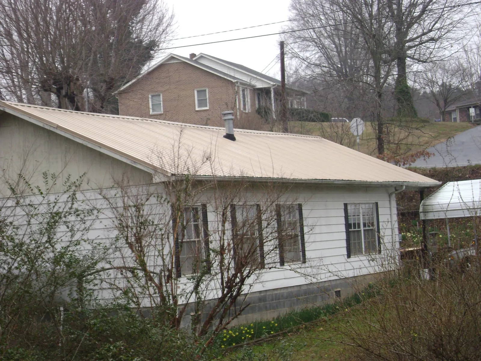 Tan metal roof on a white sided house set into a hillside — Commercial Roofing by Roofing Brothers in Reedville